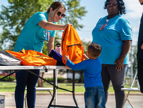 Staff member giving out backpack to child at health fair