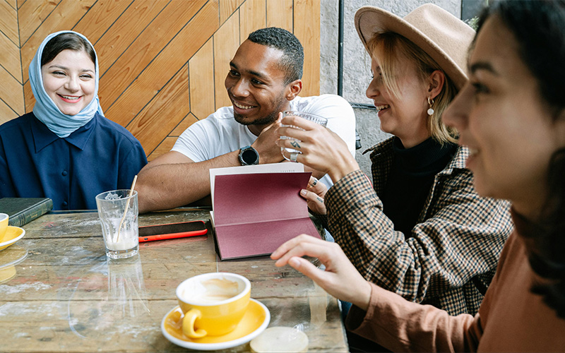 A group of people sit around a table smiling and sipping coffee