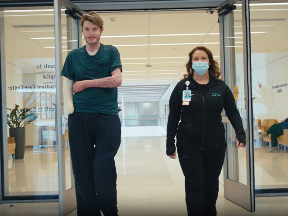 A nurse and her patient walk through a set of doors in the hallway of the hospital