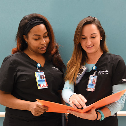 Two nurses discussing charts in a folder