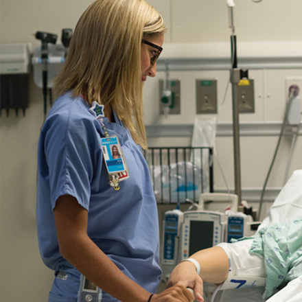 Female nurse holding the hand of a patient in a hospital bed