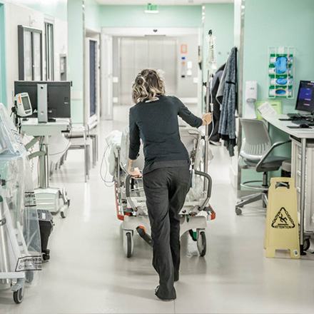 Female provider pushing a patient in a bed down the hallway
